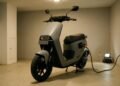 Scooter elétrica carregando em ambiente fechado, autonomia e custo de recarga da moto elétrica