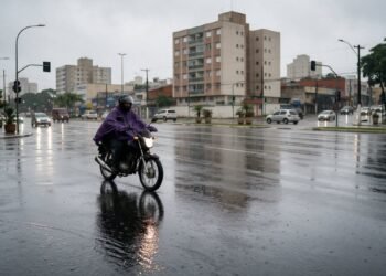 Motociclista de capa de chuva em avenida molhada da cidade