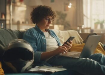 Mulher no sofá com notebook e celular avaliando se o consórcio de moto vale a pena