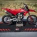 Ducati Desmo450 MX vermelha sobre tapete da Ducati Corse, com fundo de pista de terra
