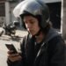 Financiamento de moto: pessoa de capacete aberto consulta o celular com uma moto estacionada ao fundo