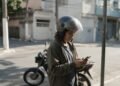 Financiamento de moto sem entrada: pessoa de capacete aberto olhando o celular com moto ao fundo