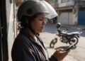 Financiamento moto Yamaha: pessoa de capacete aberto olhando o celular com moto ao fundo