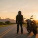 Motociclista de capacete ao lado da moto na estrada ao nascer do sol, para frases de moto motivação