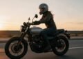 Mulher motociclista de capacete pilotando ao pôr do sol