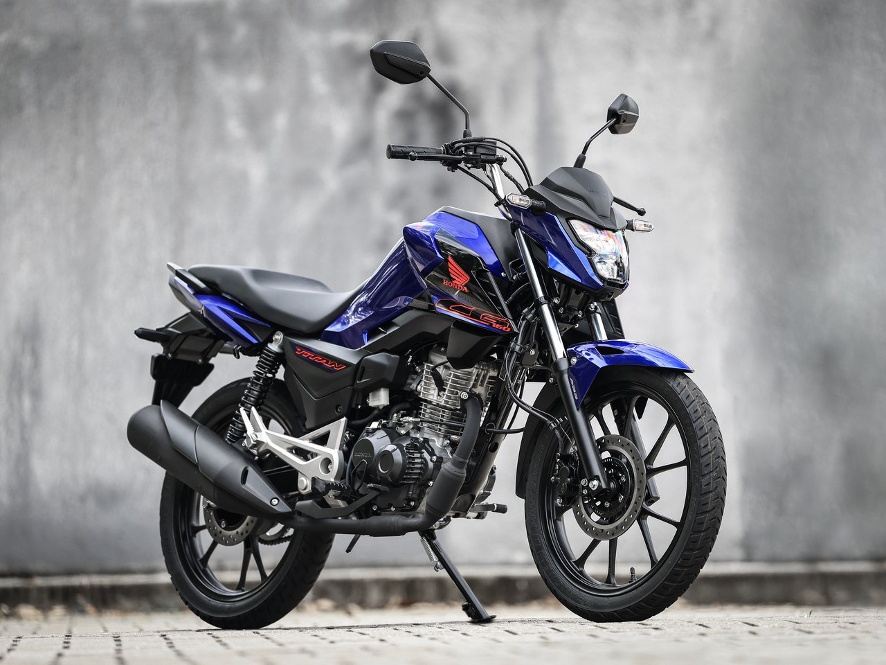 Honda Titan 2027 azul perolizado parada em frente a parede cinza