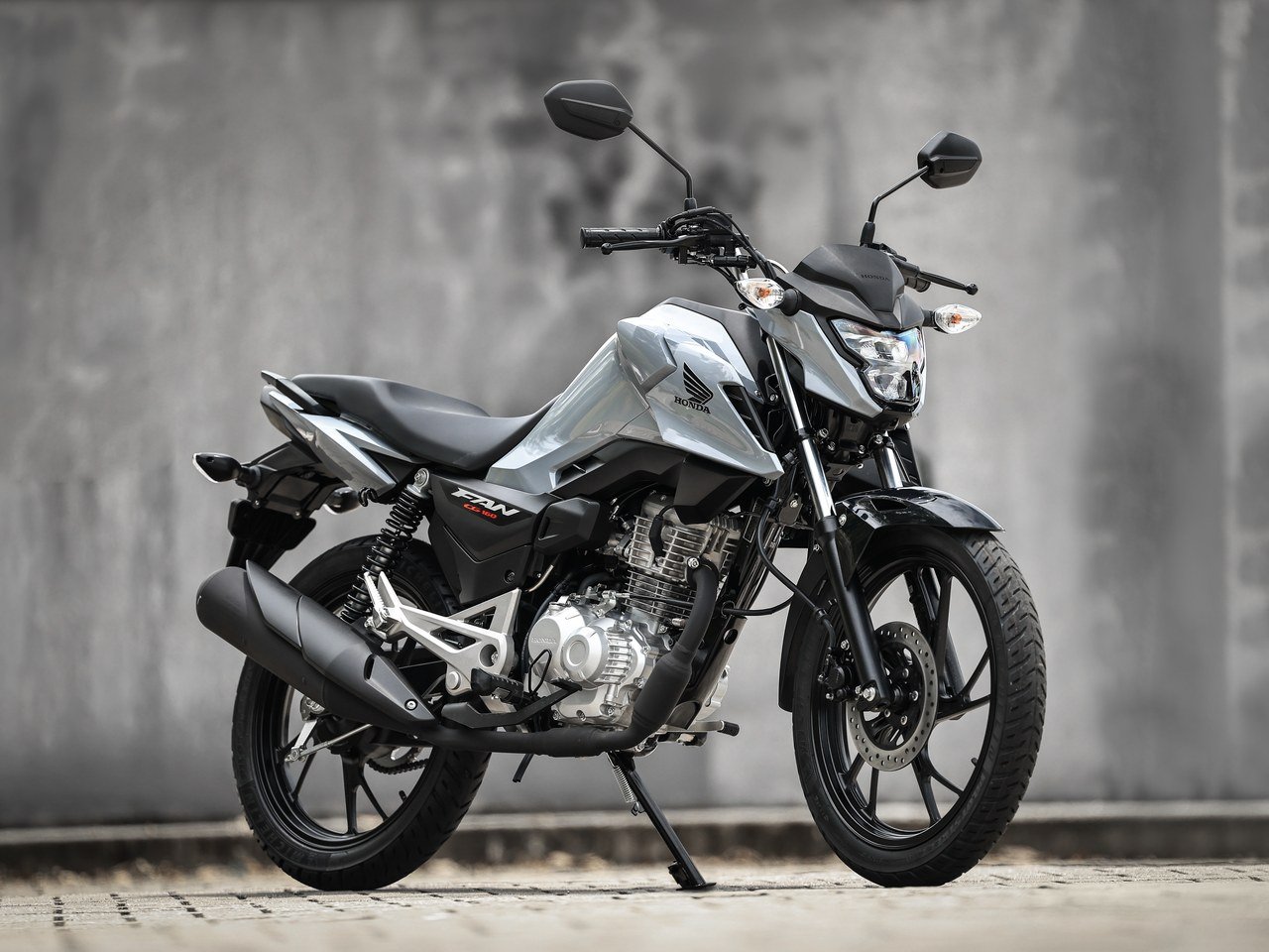 Honda CG 160 Fan 2027 cinza perolizado em vista lateral, com motor e freio a disco