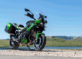 Kawasaki Versys 900 2027 verde estacionada ao lado de lago, com malas laterais e para-brisa elevado