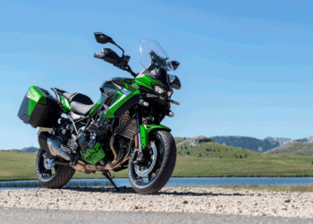 Kawasaki Versys 900 2027 verde estacionada ao lado de lago, com malas laterais e para-brisa elevado
