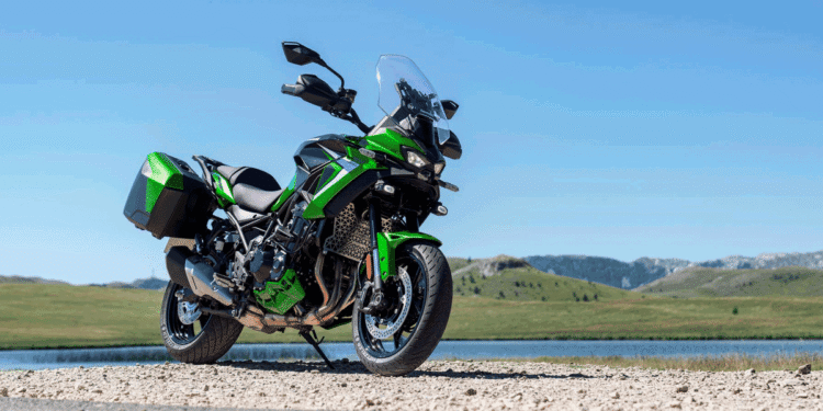 Kawasaki Versys 900 2027 verde estacionada ao lado de lago, com malas laterais e para-brisa elevado