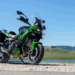 Kawasaki Versys 900 2027 verde estacionada ao lado de lago, com malas laterais e para-brisa elevado