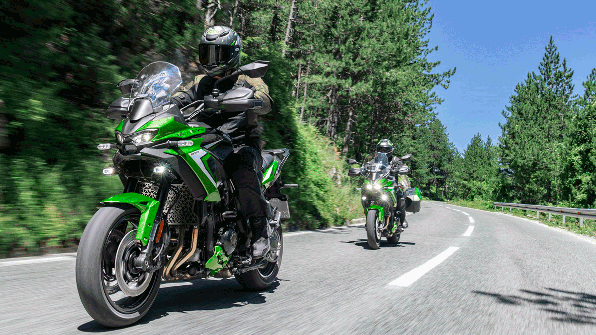 Kawasaki Versys 900 2027 verde em curva de estrada de serra, acompanhada por outra unidade da moto