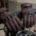 Luvas de couro com proteção nos dedos sobre o guidão de uma moto