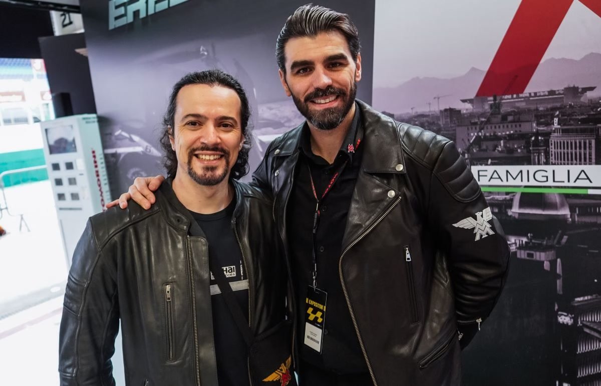 Dois integrantes da comitiva da Moto Morini posam diante do painel Famiglia no salão de Milão