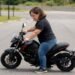 Mulher de baixa estatura apoiando os pés no chão sentada em uma moto
