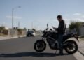 Motociclista parado olhando uma notificação de multa ao lado da moto