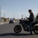 Motociclista parado olhando uma notificação de multa ao lado da moto