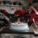 Bolo de aniversário com vela ao lado de uma moto na garagem