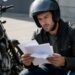 Motociclista conferindo documentos ao lado da moto, comparando proteção veicular e seguro de moto