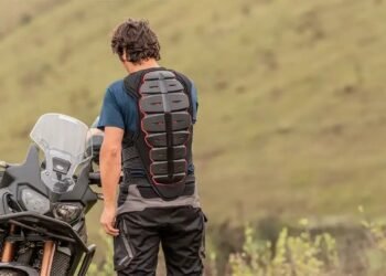 Motociclista de costas usando protetor de costas obrigatório ao lado de moto trail