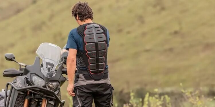 Motociclista de costas usando protetor de costas obrigatório ao lado de moto trail