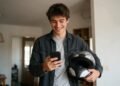 Jovem sorrindo ao ver no celular o resultado da assembleia, com capacete de moto na mão