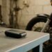 Rastreador compacto em oficina com moto ao fundo, rastreador com bloqueio para moto