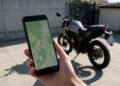 Mão segurando celular com mapa e moto ao fundo, rastreador de moto pelo celular