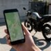Mão segurando celular com mapa e moto ao fundo, rastreador de moto pelo celular