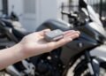 Mini rastreador na mão com moto ao fundo, rastreador portátil para moto