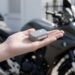 Mini rastreador na mão com moto ao fundo, rastreador portátil para moto