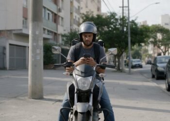 Motorista de aplicativo em cima da moto olhando o celular, representando seguro de moto para aplicativo