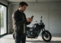 Motociclista consulta no celular o seguro moto Porto Seguro, ao lado da moto na garagem